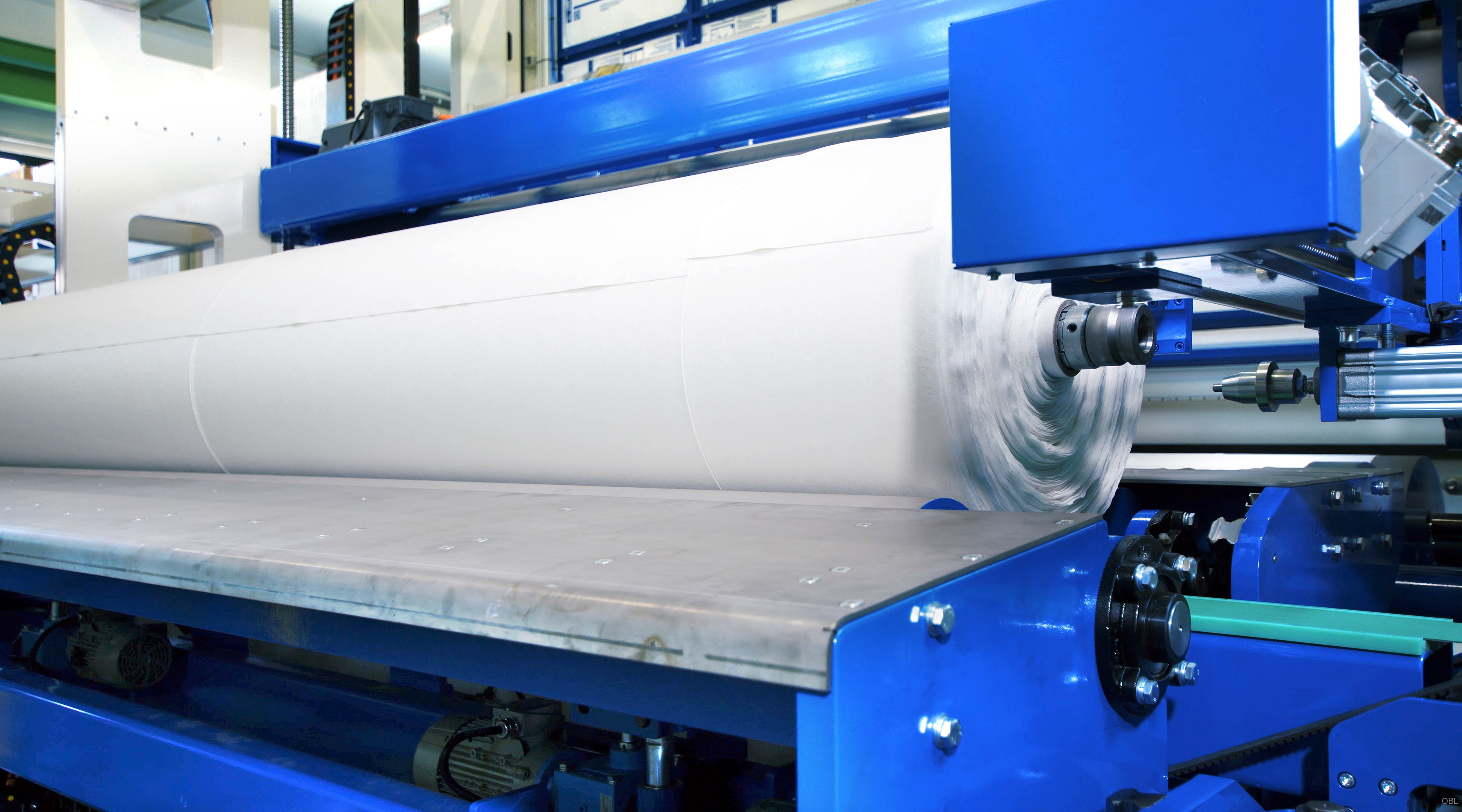 A shuttle machine is specialized equipment used for moving and processing various materials, typically in an industrial setting such as production or packaging. In this image you can see the machine at work, demonstrating its operation. The main focus of the image is on the rollers attached to the shuttle machine. These are large cylindrical components that facilitate the handling and processing of the material within the system. The surface of the roller appears smooth and well cared for, ensuring clean contact with the materials being processed. Furthermore, it is possible to observe other mechanical parts connected to these rollers via various arms or levers, which contribute to the overall functioning of the shuttle machine. These components likely play a role in guiding, lifting, or otherwise manipulating the material as it passes through different phases within the processing area. In summary, this image shows a Shuttle Machine actively engaged in its function, highlighting the key